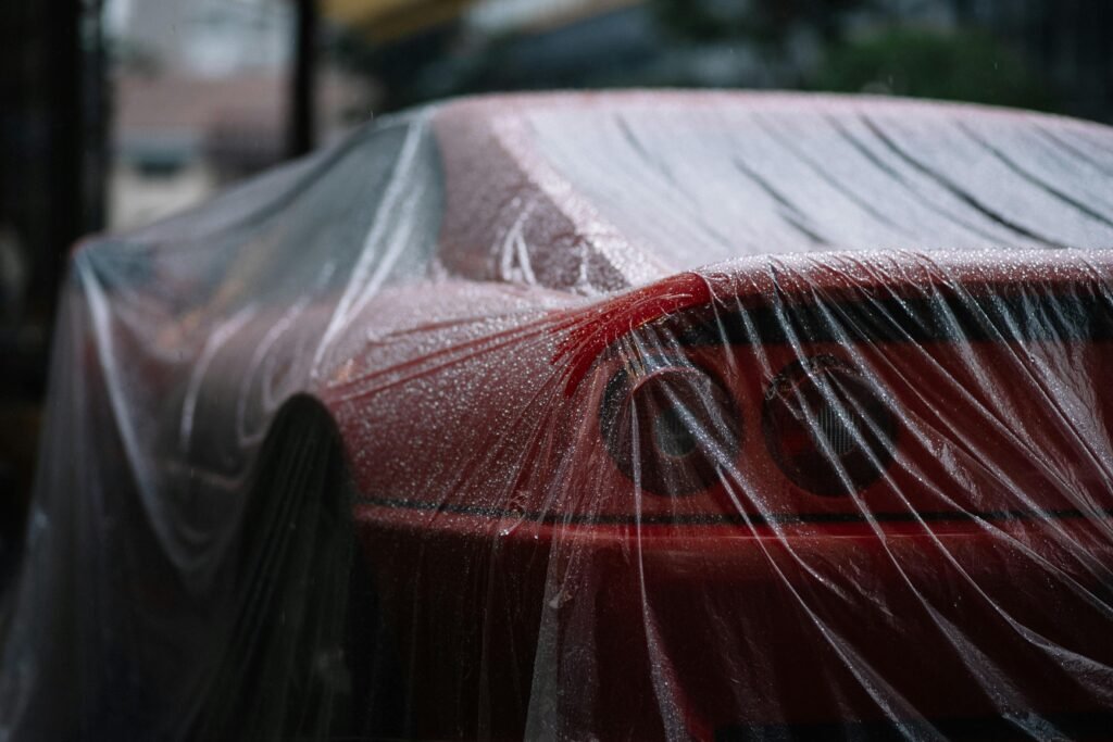 Close-up of a red sports car covered with wet foil, highlighting raindrops and sleek design.